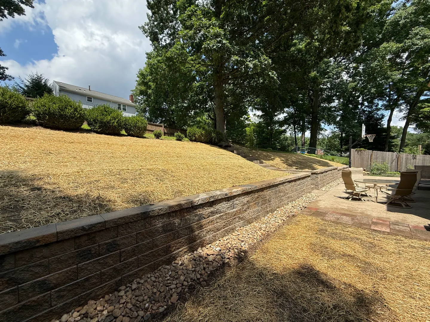 Curved block retaining wall holding a seeded hillside above a paver patio