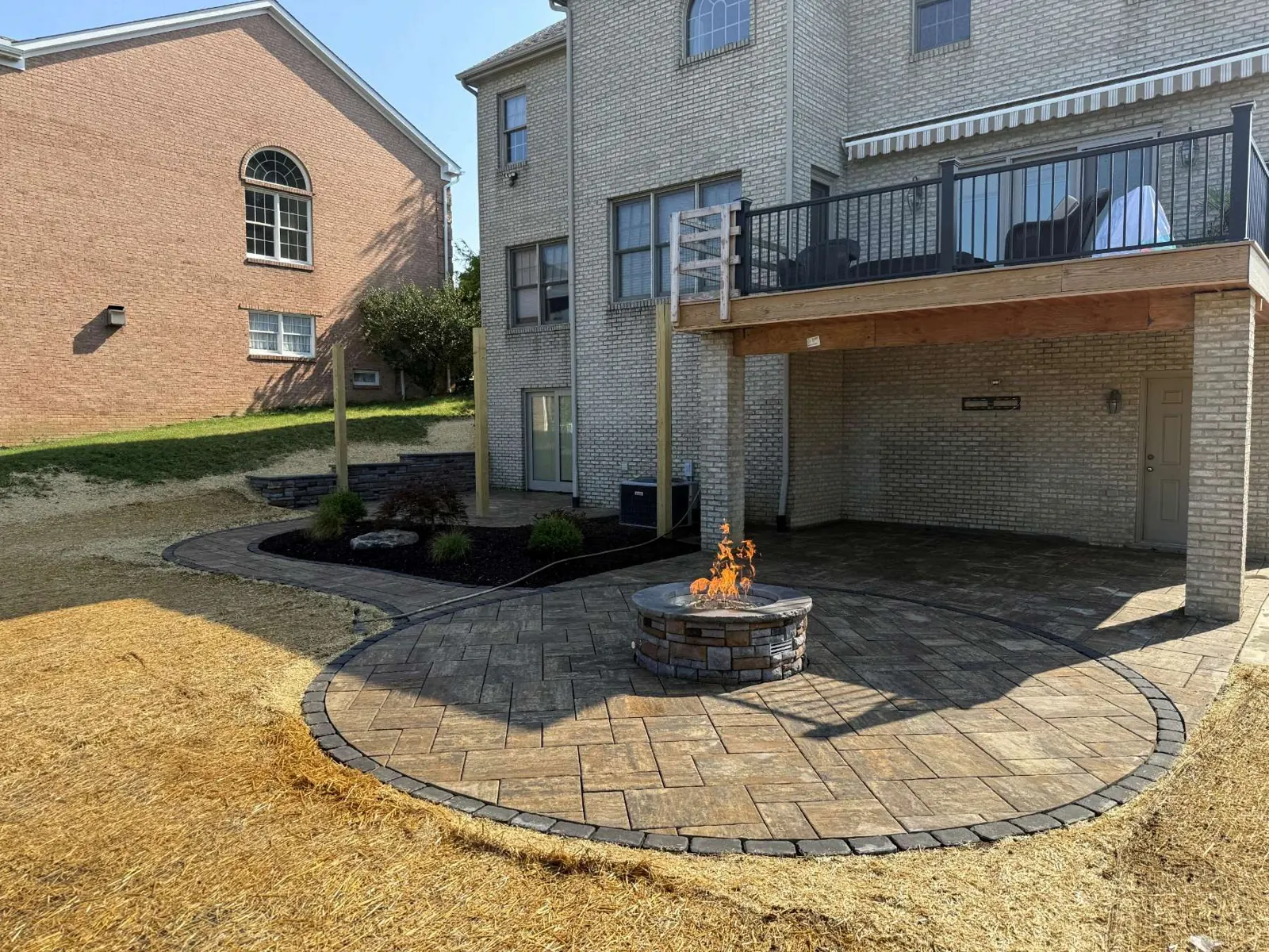 Extra large round paver patio with a lit firepit beneath a deck