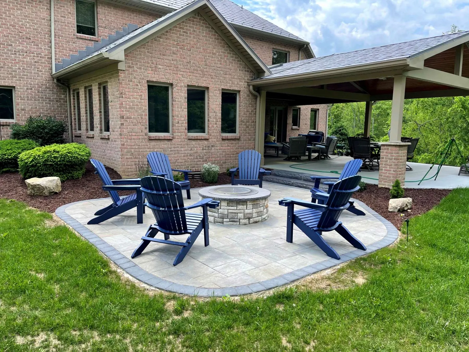 Medium paver patio with a curved edge, border paver, and a stone firepit with Adirondack chairs