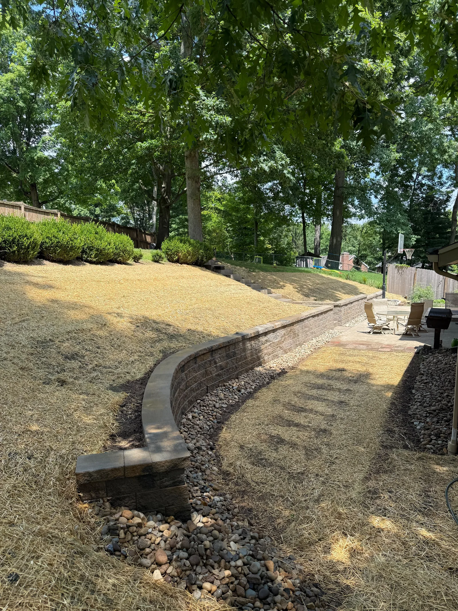 Curved Versa-Lok wall in the backyard with river rock at its base and the patio beyond it