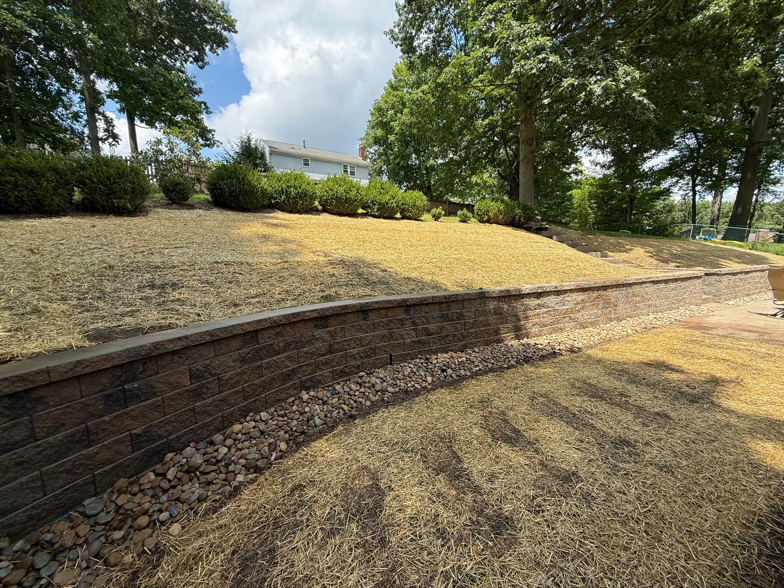 Long Versa-Lok wall along the backyard slope with river rock at its base