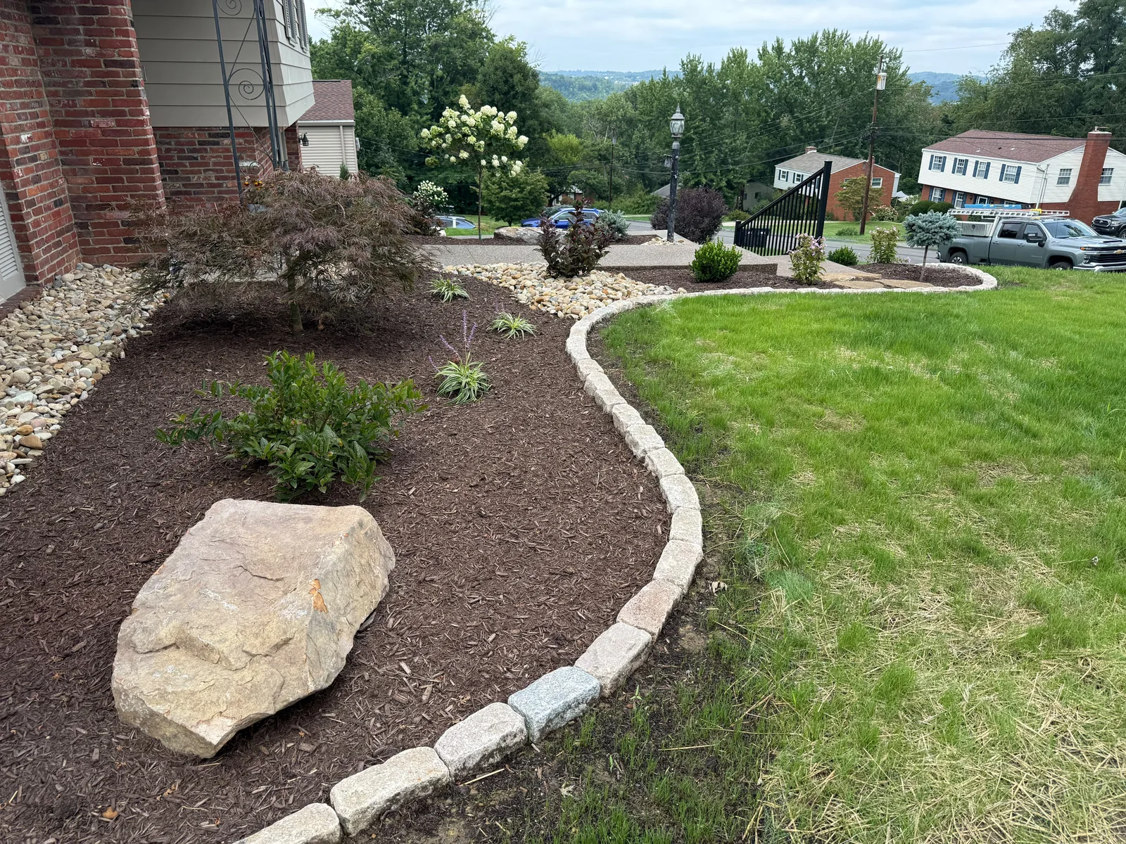 Curved mulch bed with a boulder and shrubs, edged with Belgian block along the lawn