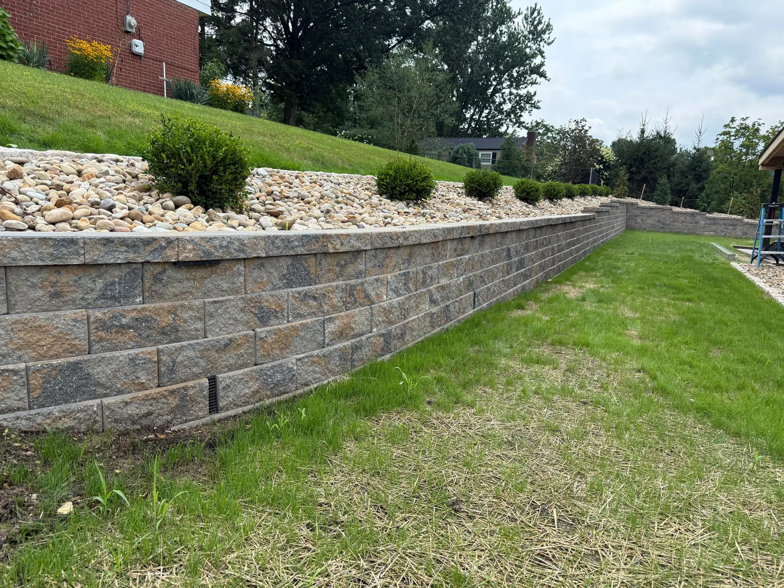 Long new Versa-Lok wall along the lawn, with river rock and shrubs along the top