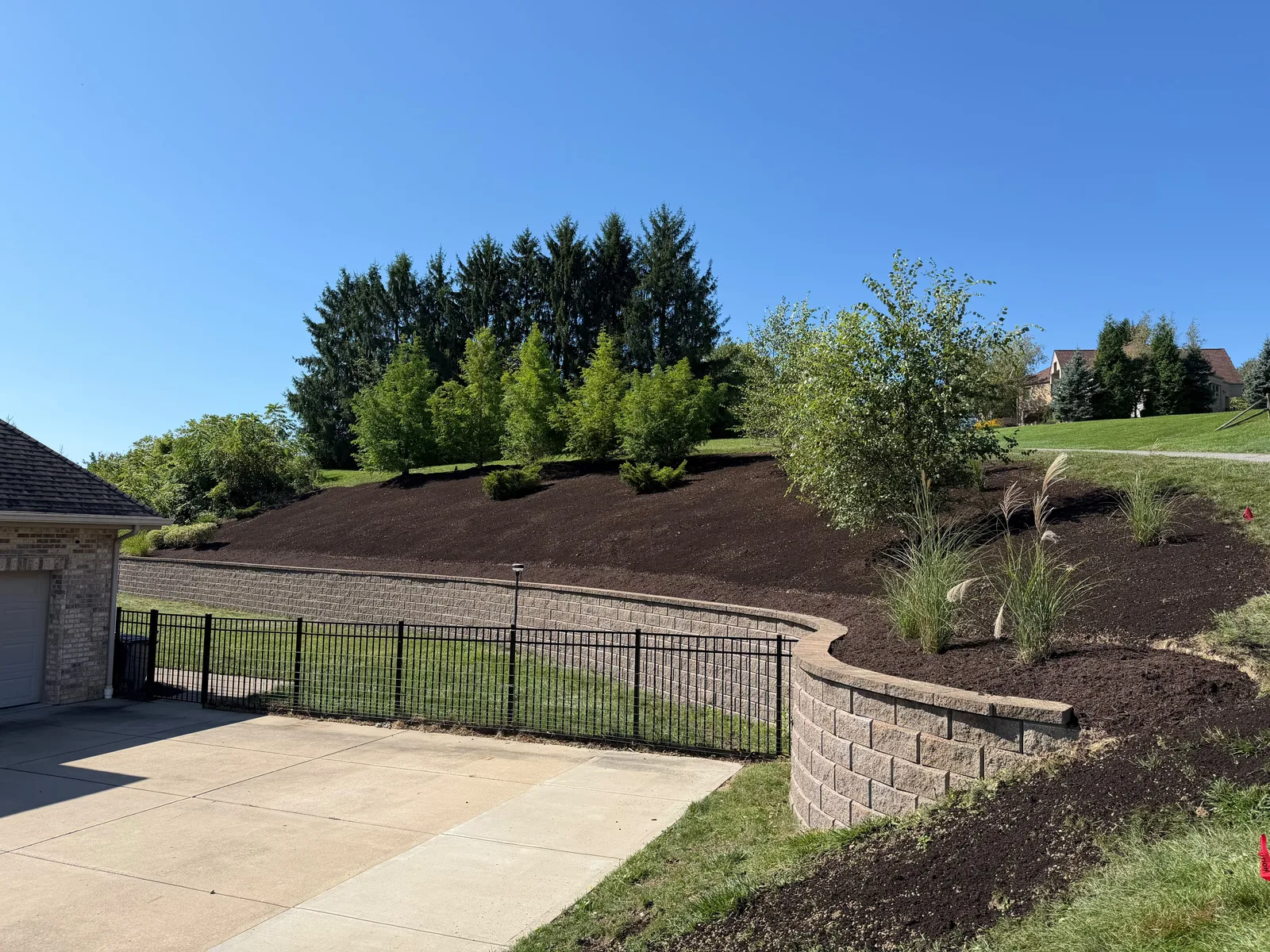 Fresh brown mulch over the hillside bed above a retaining wall and black fence at a Venetia home