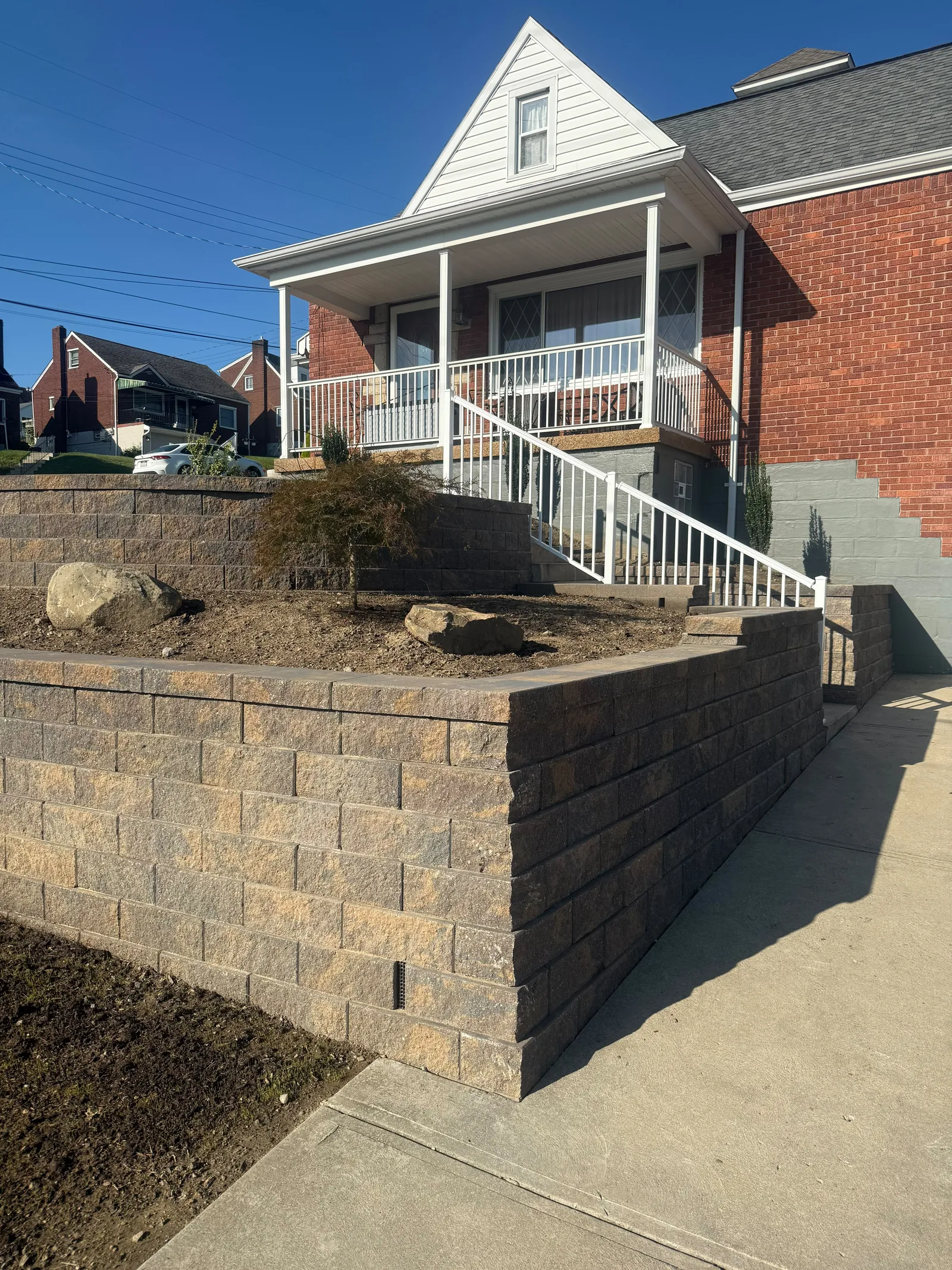 New Versa-Lok wall and the white railing along the front steps, with boulders and a small tree in the bed