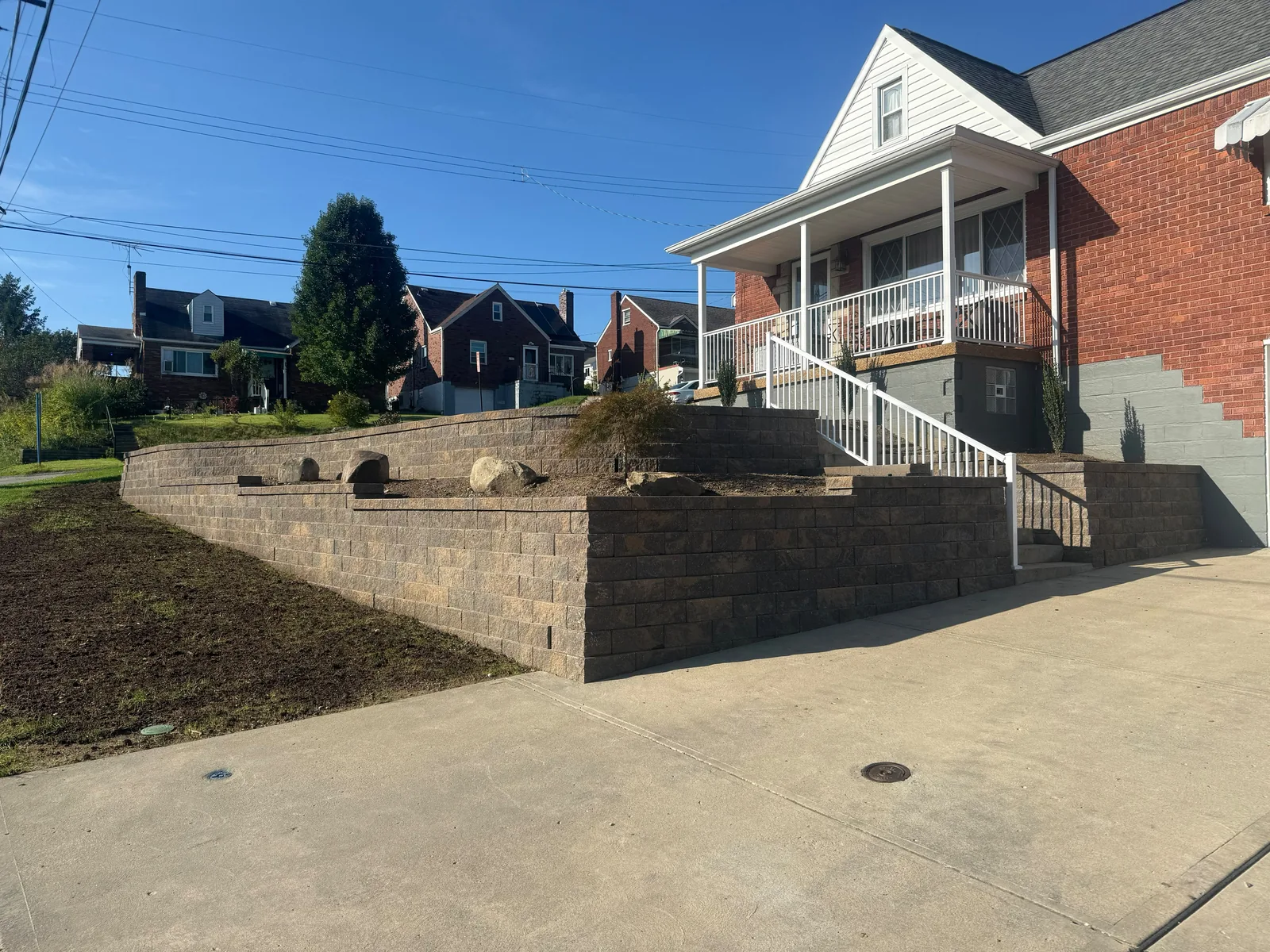 New Versa-Lok retaining walls, front steps with a white railing, and the driveway at a West Mifflin home